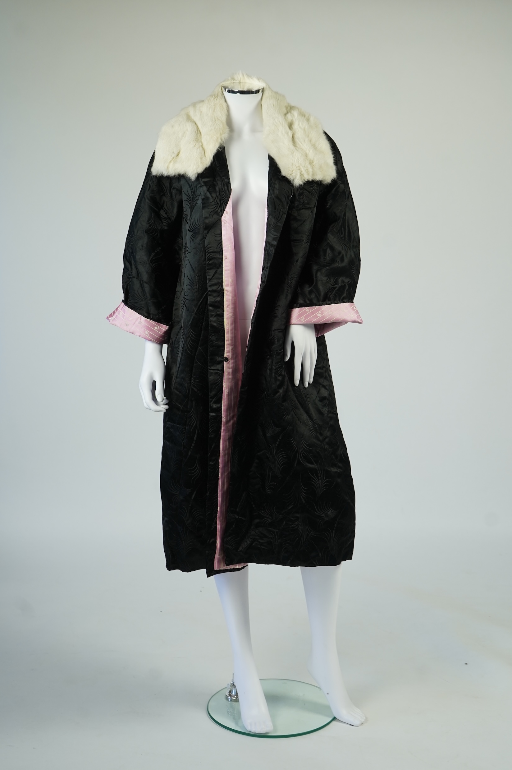 A 20th century ladies black silk damask opera coat, trimmed with a white fur collar and pink silk stripe brocade lining. 116cm from shoulder to hem. Condition - seams unstitched in places, small nick to black brocade by